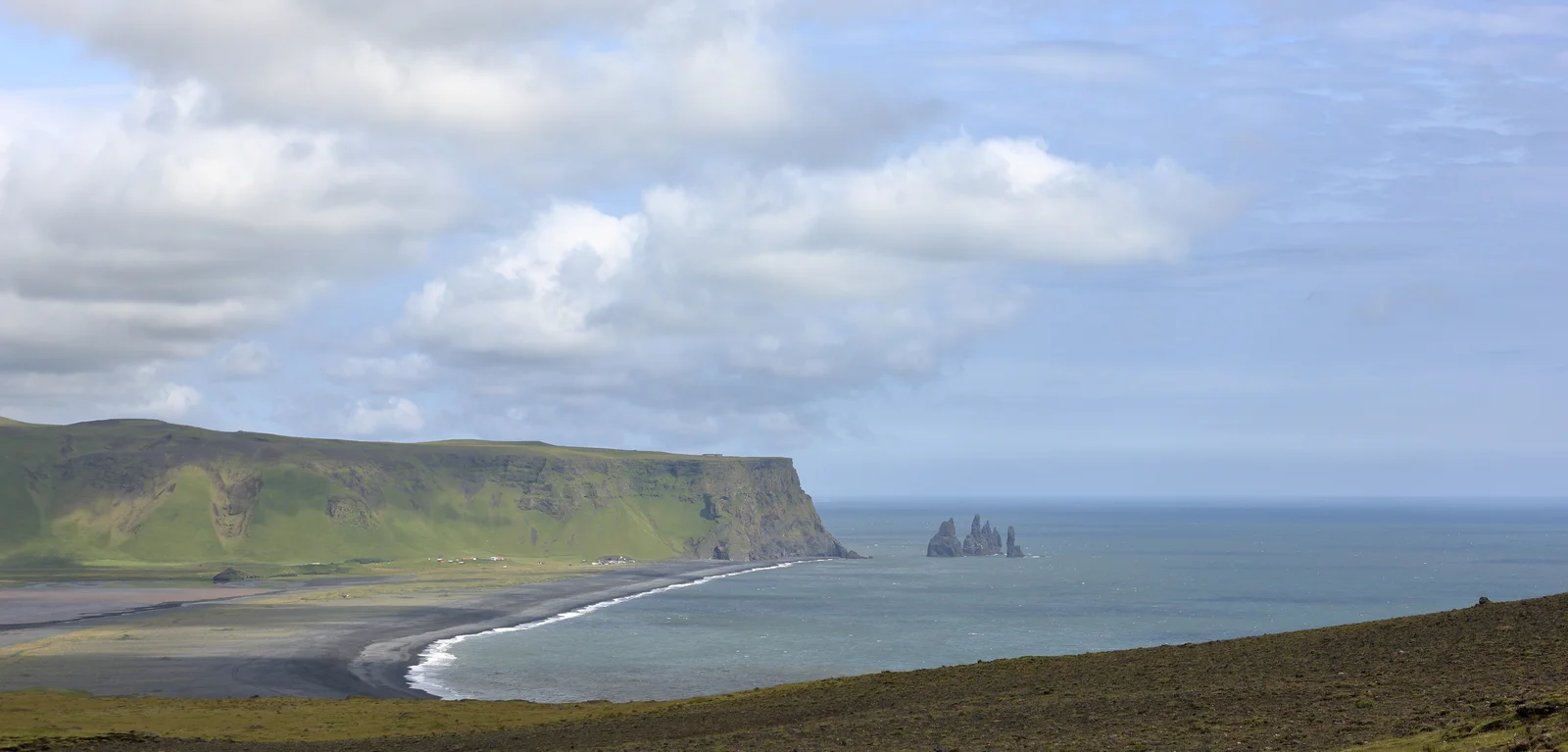 The black basalt sands of Reynisfjara beach with the Reynisdrangar sea stacks rising offshore near Vík