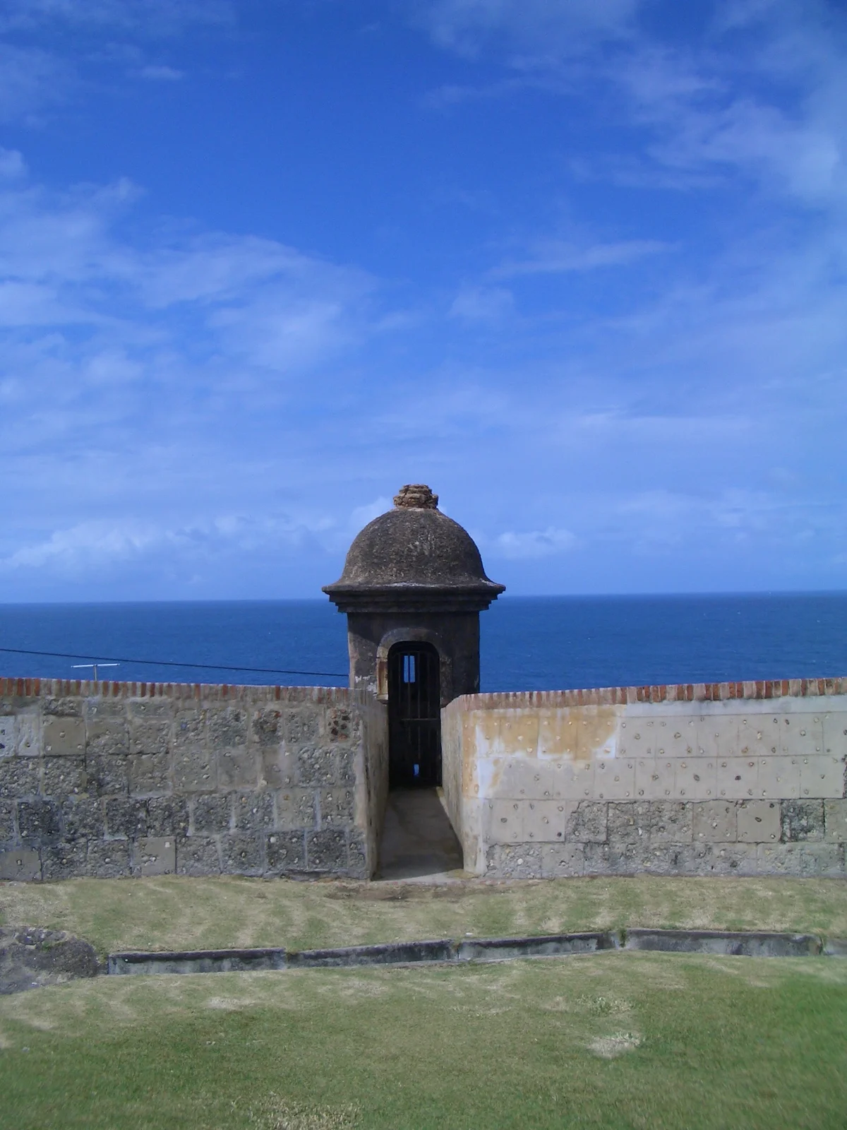 A domed stone garita sentry box built into El Morro's low seaward wall, its arched doorway open, with the open Atlantic on the horizon and a grassy slope in front