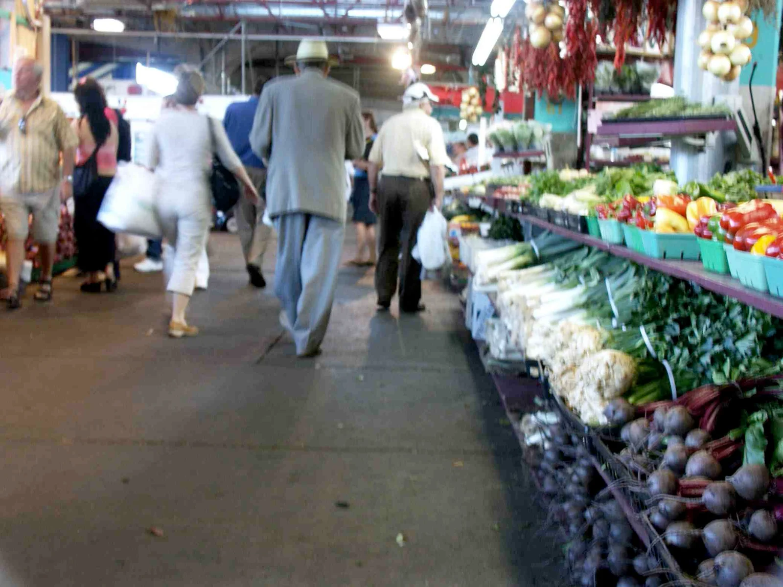 Shoppers walking down an aisle inside the covered hall of Jean-Talon Market past a long vegetable display