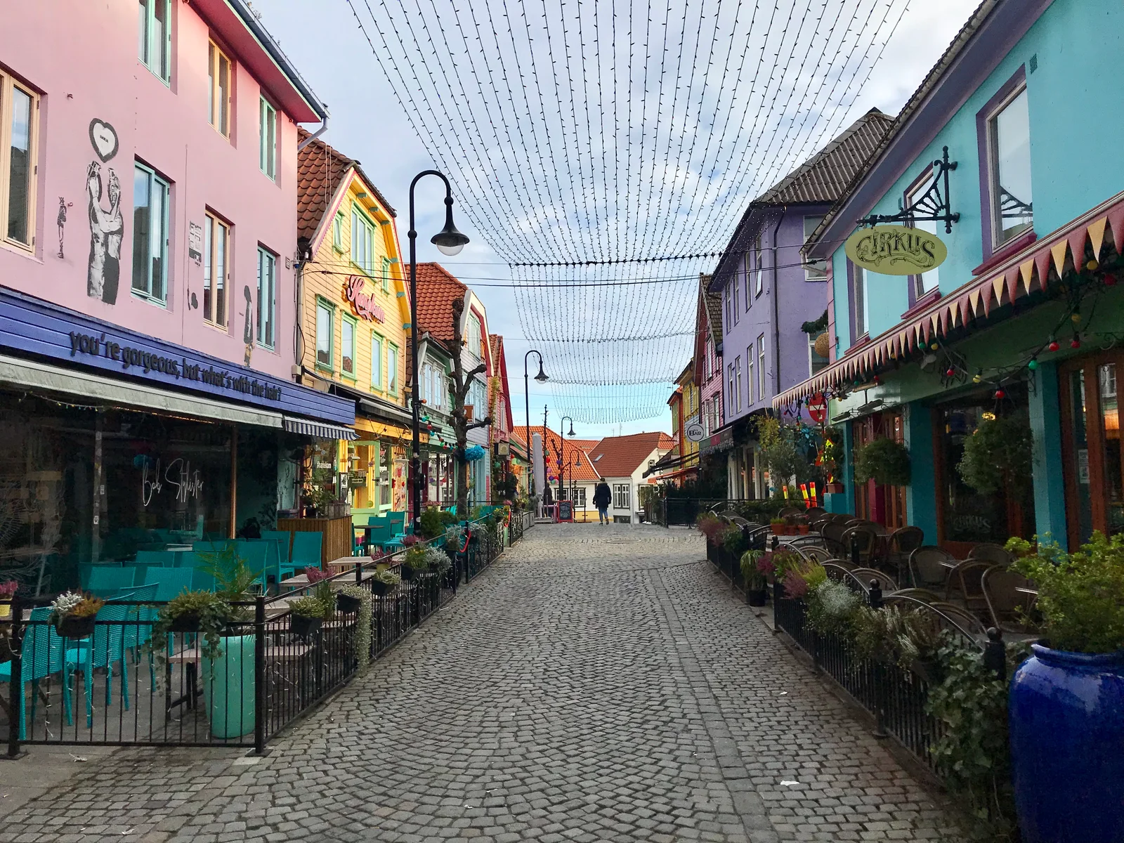 The cobbled Ovre Holmegate lined with buildings painted pink, yellow, purple and blue, strings of lights strung overhead