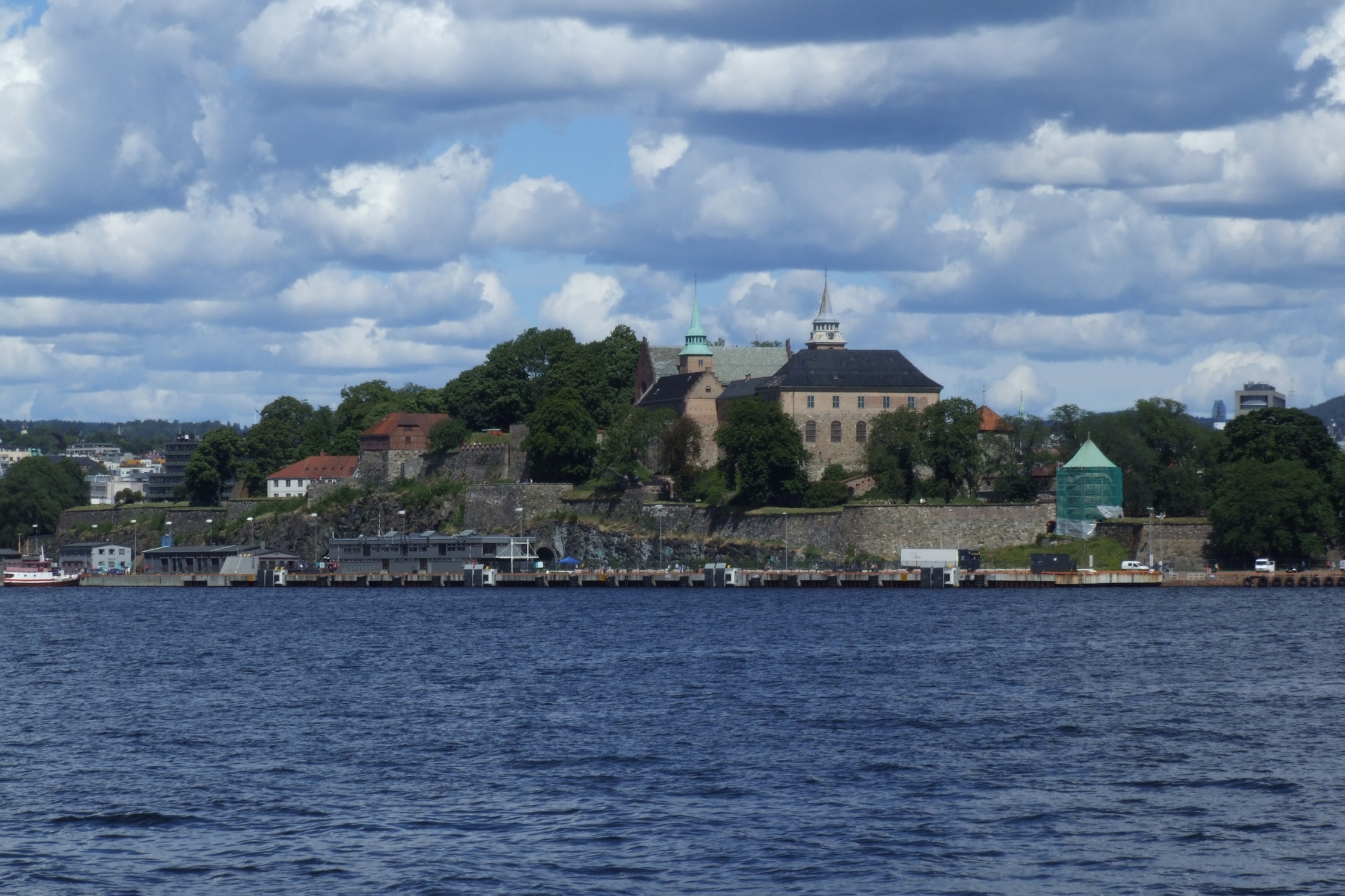 Akershus Fortress medieval stone walls and towers rising above the Oslo fjord, with the harbour and Aker Brygge visible in the background