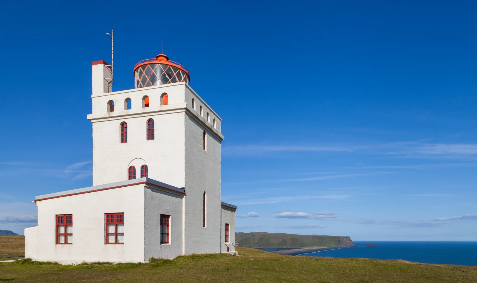The white Dyrhólaey lighthouse standing on its high cliff above the black-sand coast of south Iceland