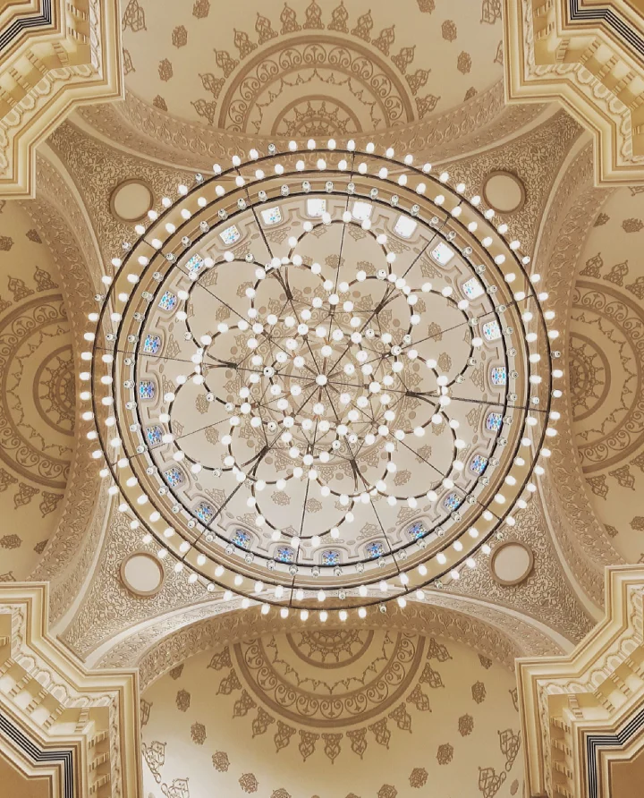 Looking straight up into Al Noor Mosque's central dome at its circular chandelier and gold arabesque plasterwork