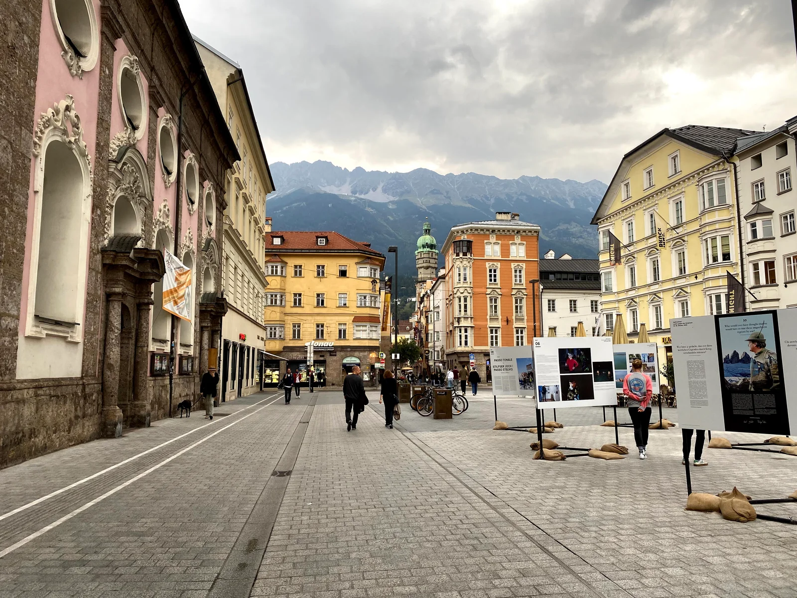 The wide pedestrianised Maria-Theresien-Strasse lined with pastel baroque facades, leading toward the grey crags of the Nordkette range under an overcast sky