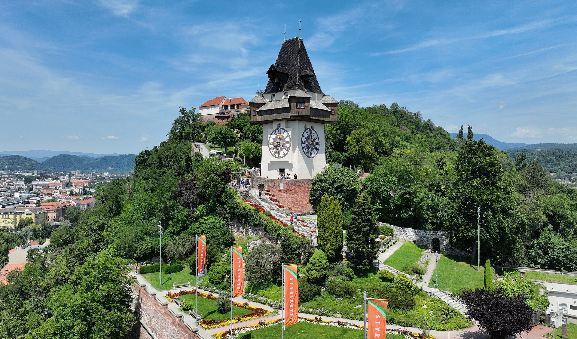 The Uhrturm clock tower on the Schlossberg in Graz, a white medieval tower with its famously reversed clock hands surrounded by green trees