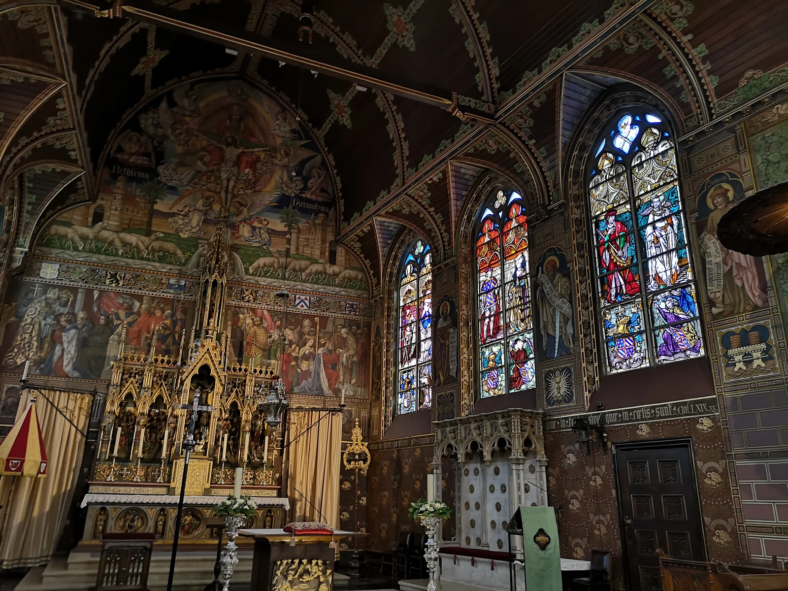 Ornate upper chapel with wall murals, a gilded neo-Gothic altar and tall stained-glass lancet windows