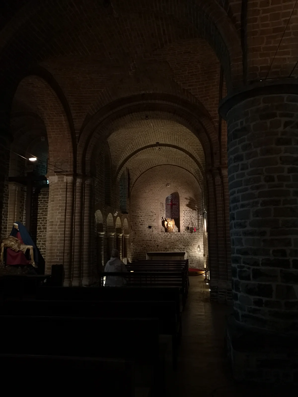 Dim, brick barrel-vaulted nave of the lower St. Basil's Chapel with wooden pews facing a lit niche