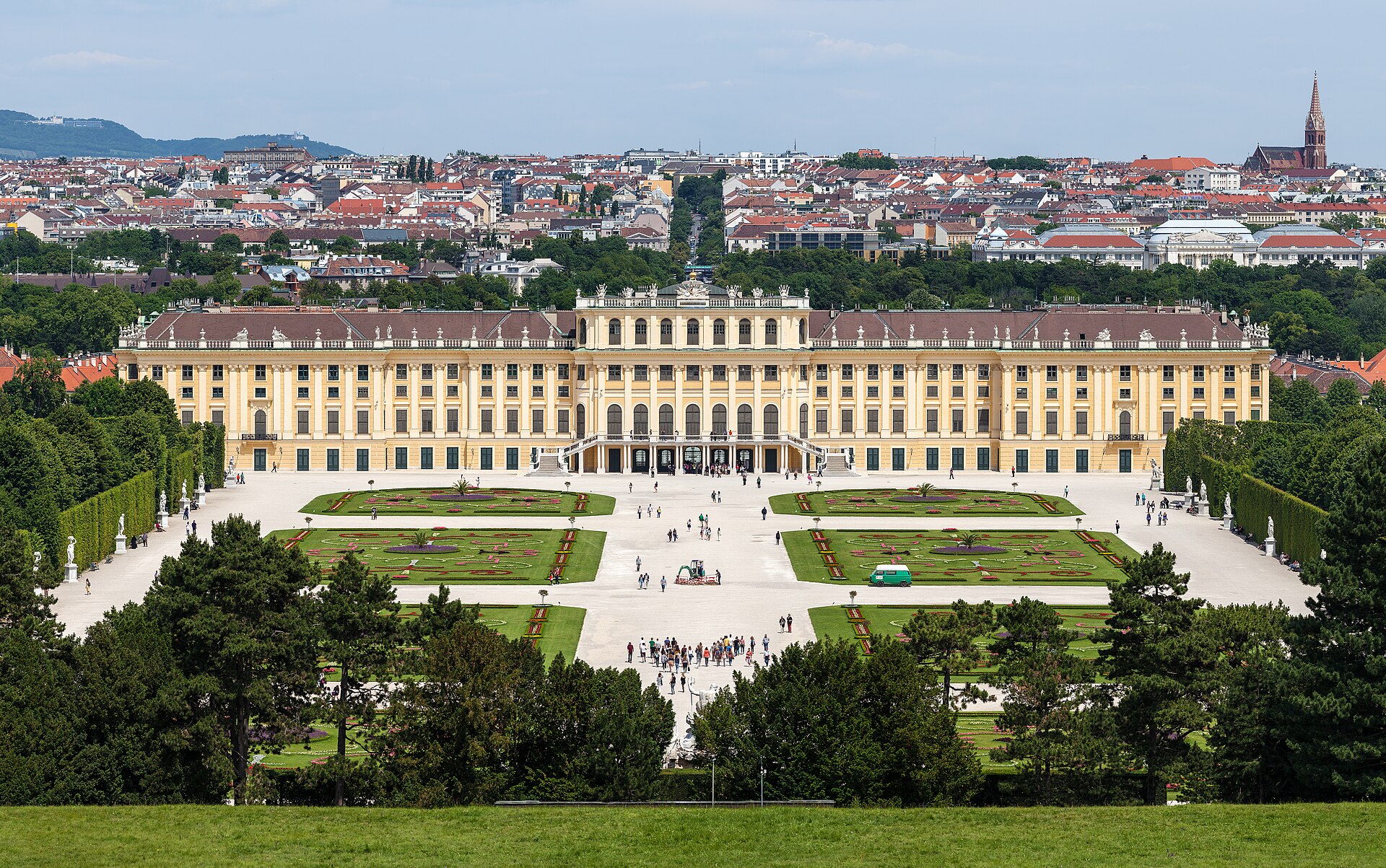 Front facade of Schoenbrunn Palace in Vienna seen from the Great Parterre garden, with the golden-yellow baroque building under a dramatic sky