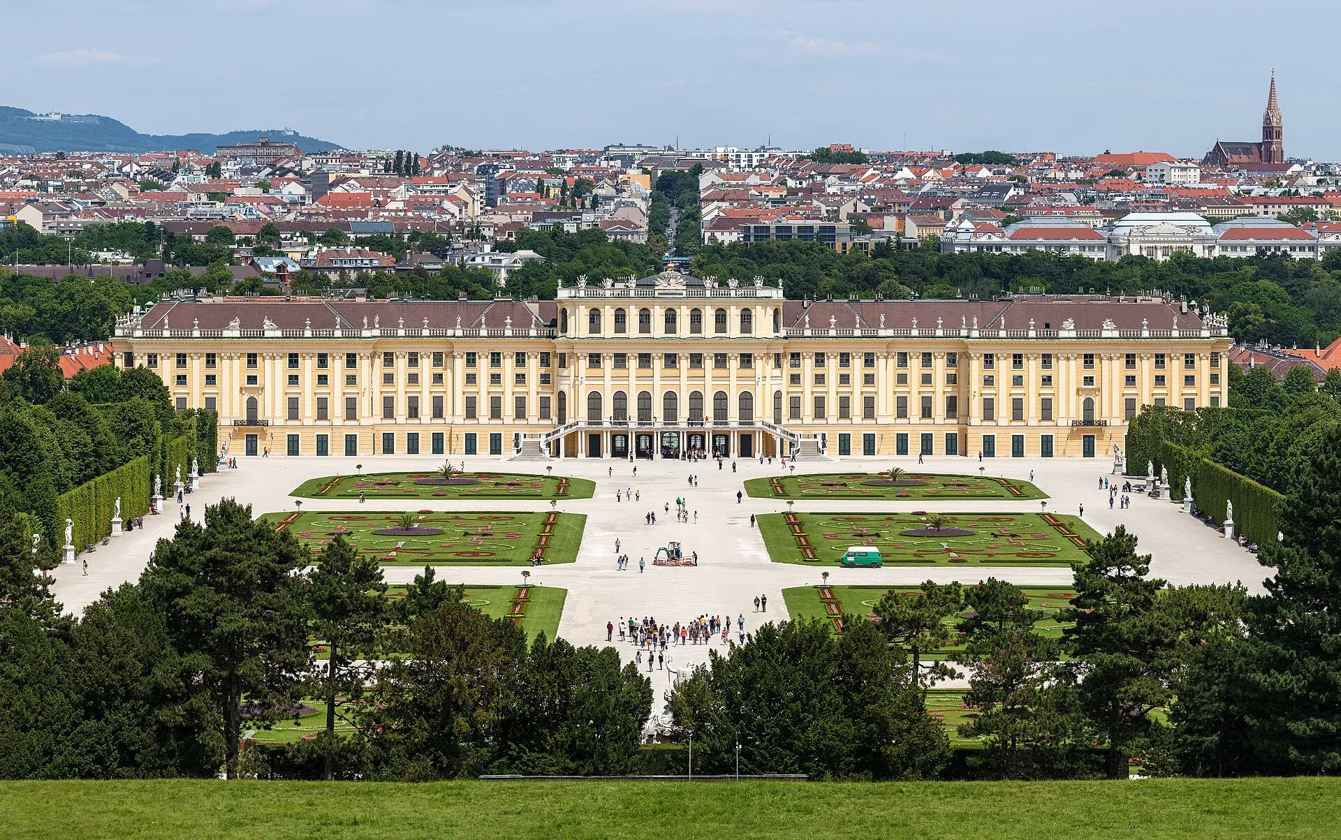 Schoenbrunn Palace's golden-yellow baroque facade in Vienna, seen from the Great Parterre garden under a dramatic sky
