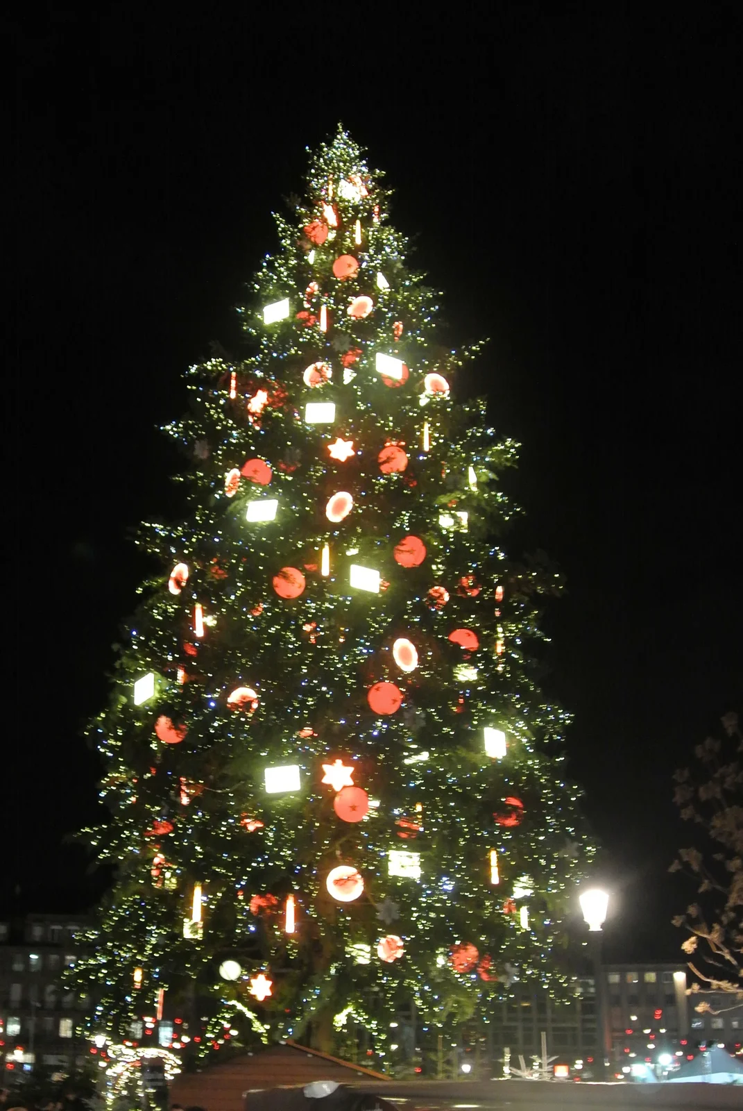 Strasbourg's tall illuminated Christmas tree at night on Place Kléber, hung with large red baubles and white lights