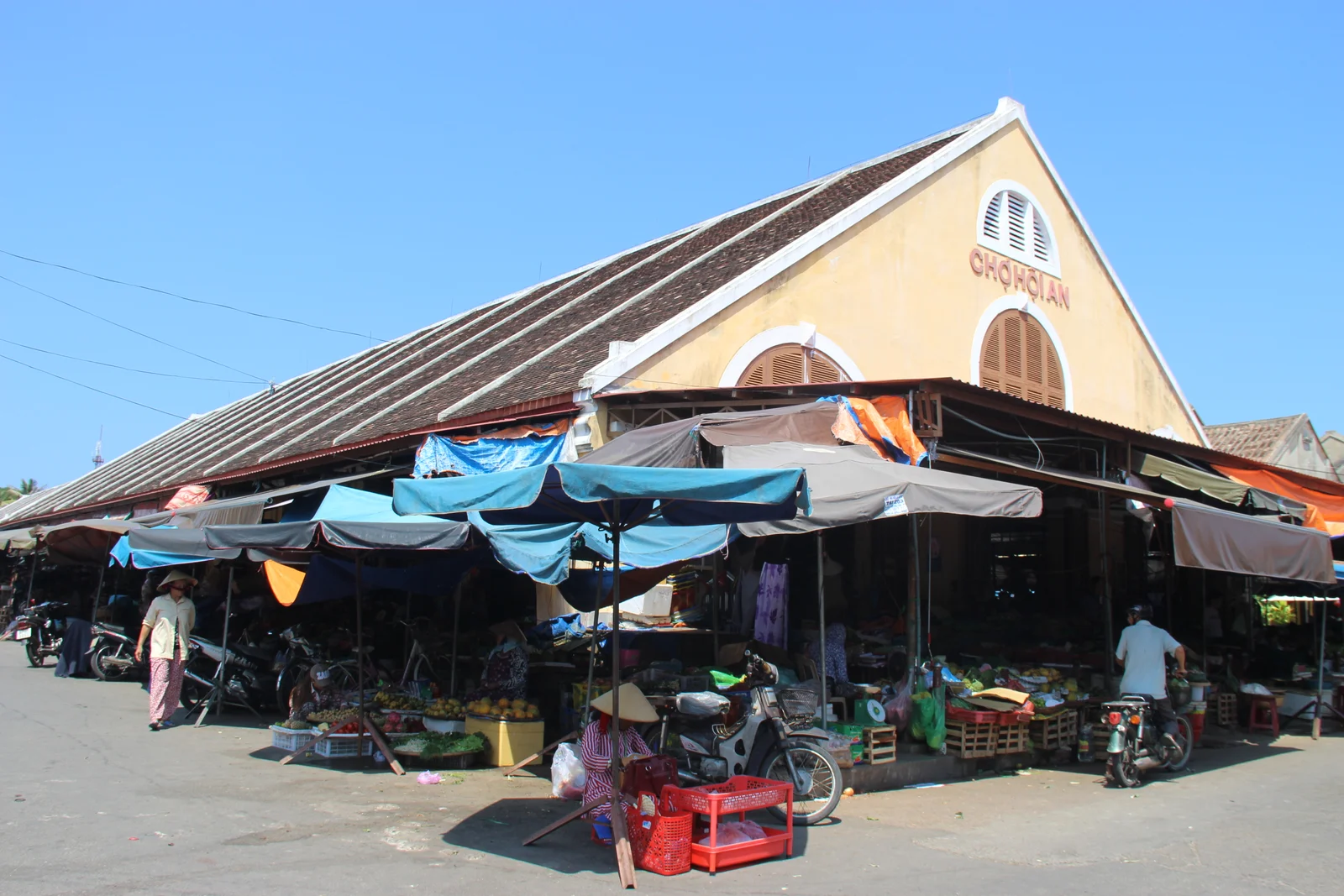 The ochre gabled hall of Hoi An's central market, its name painted on the pediment above tarpaulin-shaded produce stalls