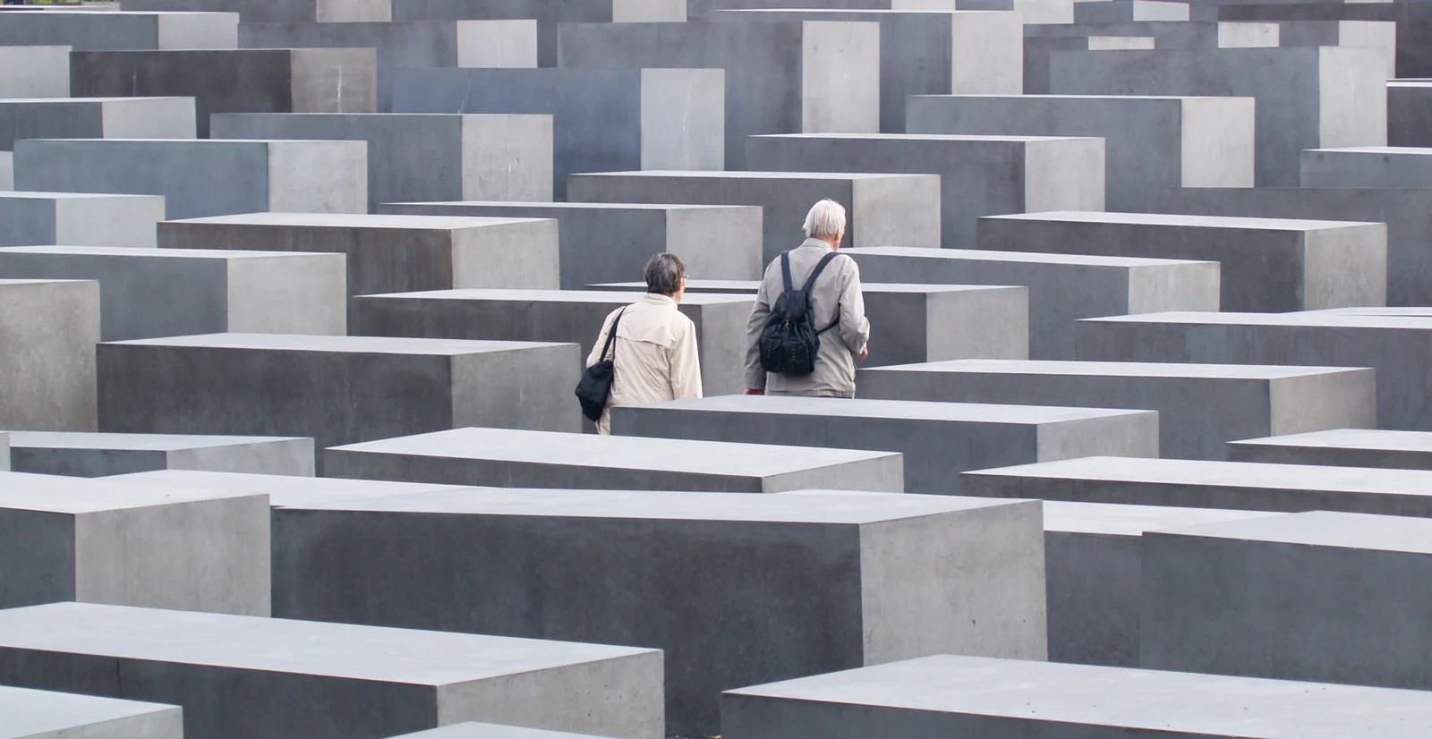 An elderly couple walking between rows of grey concrete stelae at Berlin's Holocaust Memorial