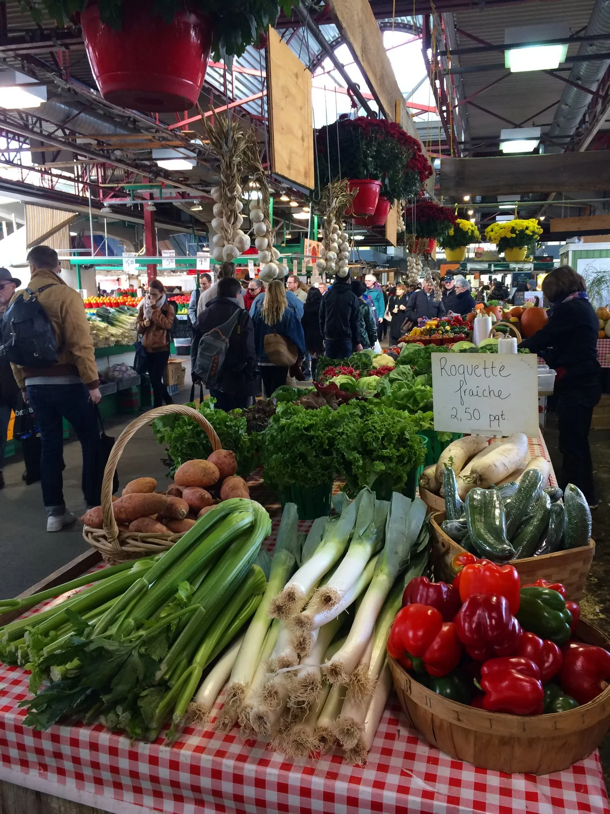 Market stall table of leeks, celery, sweet potatoes, peppers and cucumbers with a handwritten arugula price sign