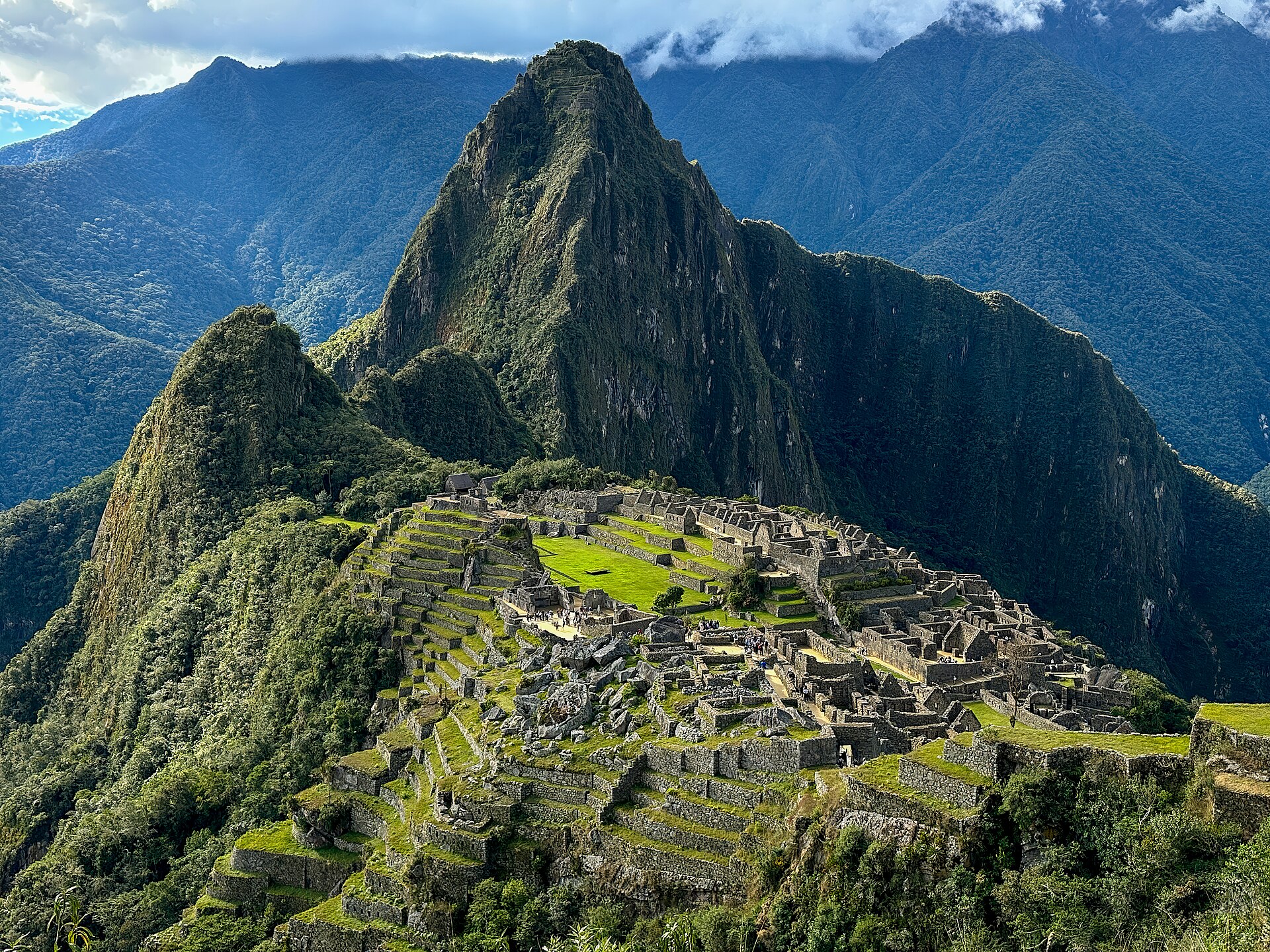 Classic postcard view of Machu Picchu ruins with Huayna Picchu mountain rising in the background under a partly cloudy sky