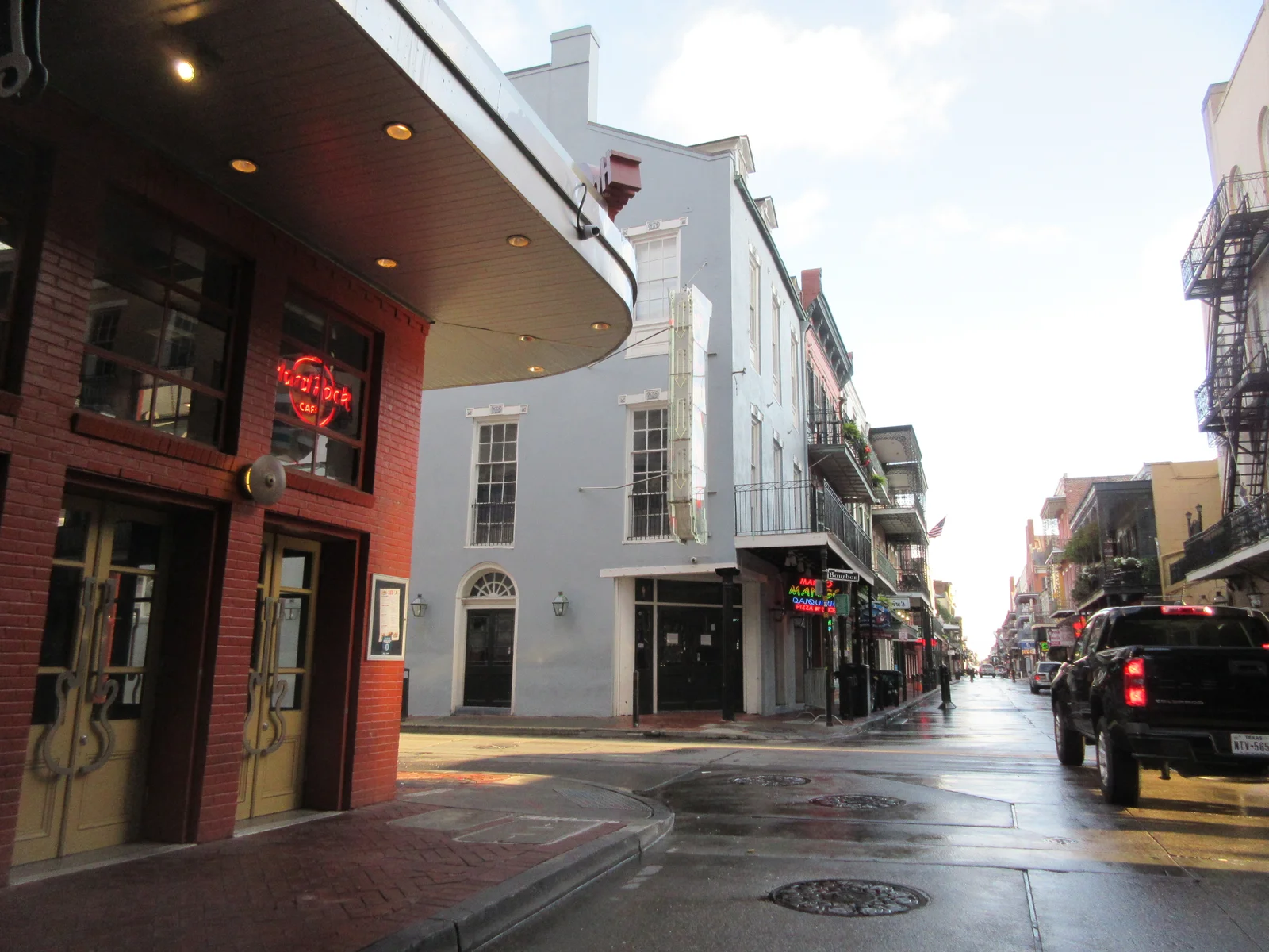 Quiet, rain-slicked Bourbon Street on a weekday morning, the red-brick Hard Rock Cafe corner on the left and cast-iron balconies lining the block ahead