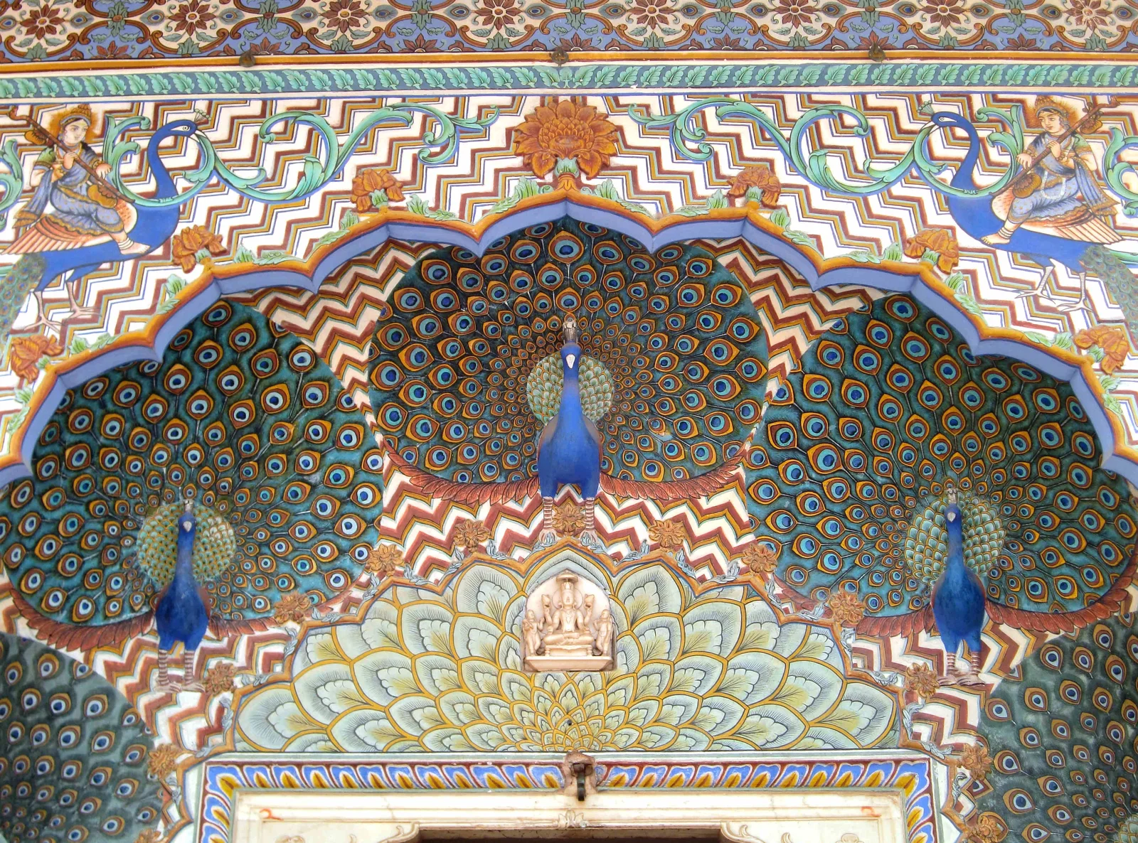 Close-up of the Peacock Gate's painted archway at Jaipur's City Palace, with iridescent blue peacocks fanning their tails around a scalloped, lotus-painted arch