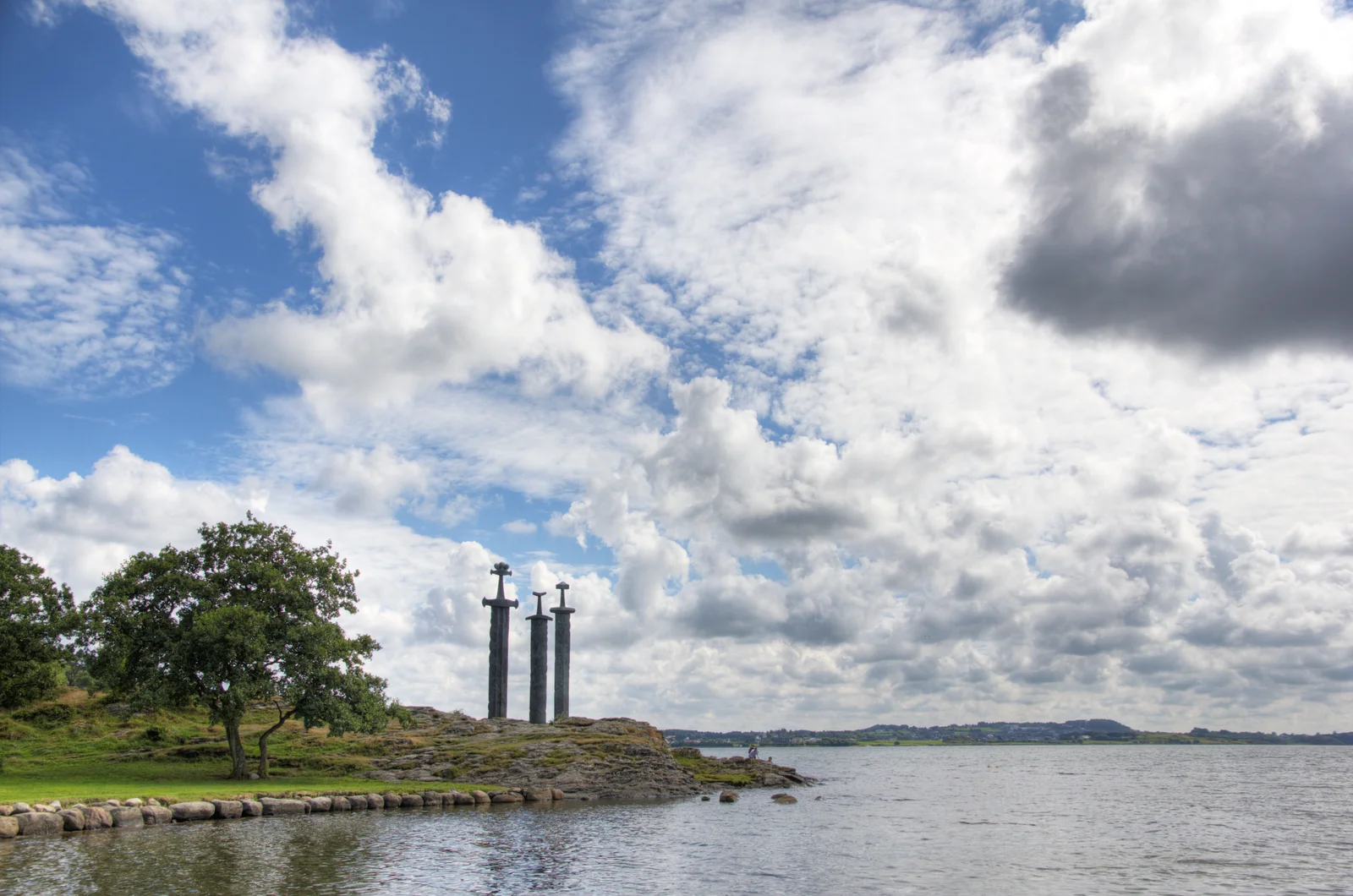 The three tall bronze swords of the Sverd i fjell monument planted in a rocky point beside Hafrsfjord
