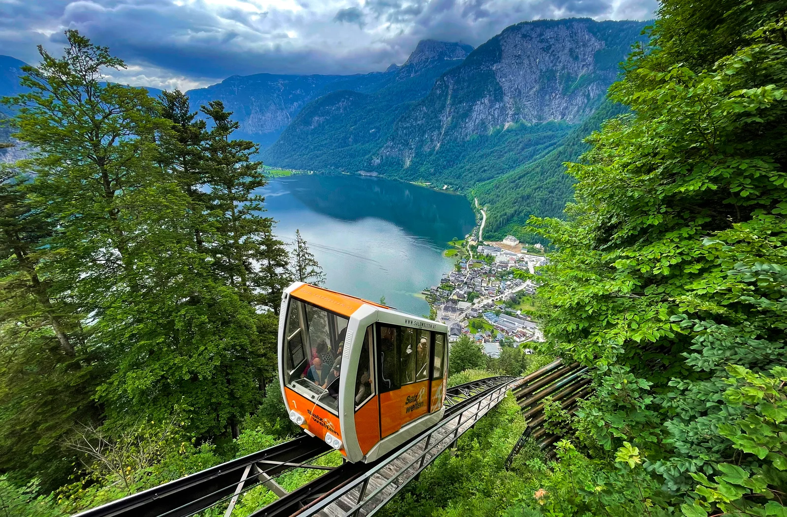 A Salzbergbahn funicular car climbing the steep forested Salzberg slope above Hallstatt with the Hallstättersee lake in the background