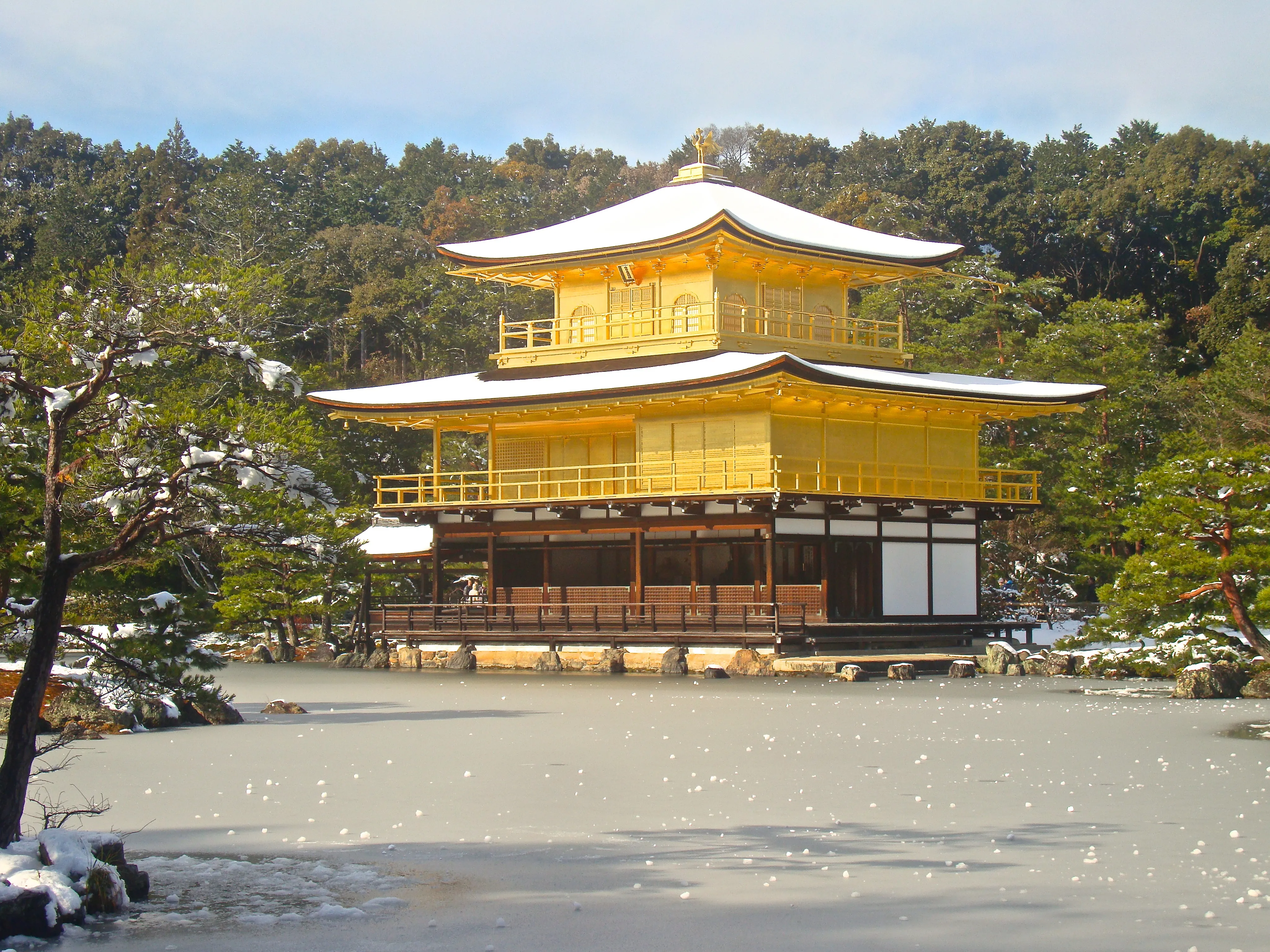 The Golden Pavilion of Kinkaku-ji dusted with snow above its frozen reflecting pond in winter