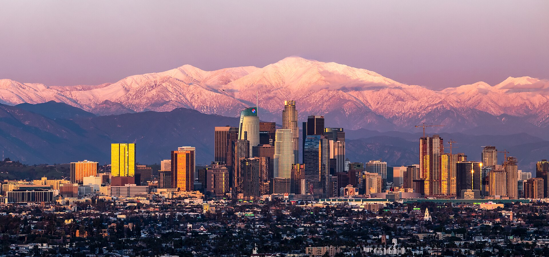 Downtown Los Angeles skyline at sunset with snow-capped Mount Baldy in the background
