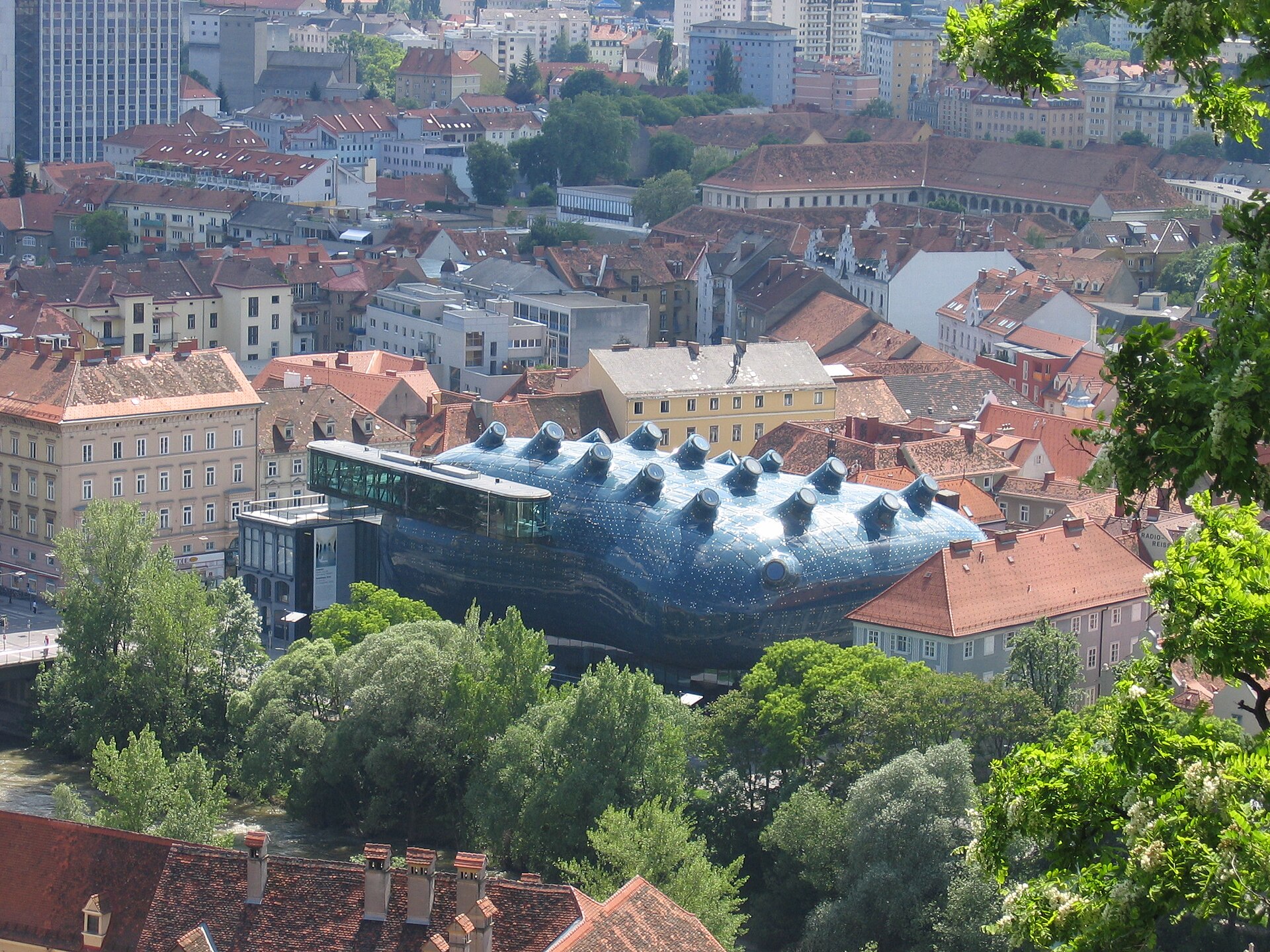 The Kunsthaus Graz, a blob-shaped modern art museum with its distinctive blue acrylic-panel skin contrasting with traditional buildings along the Mur River