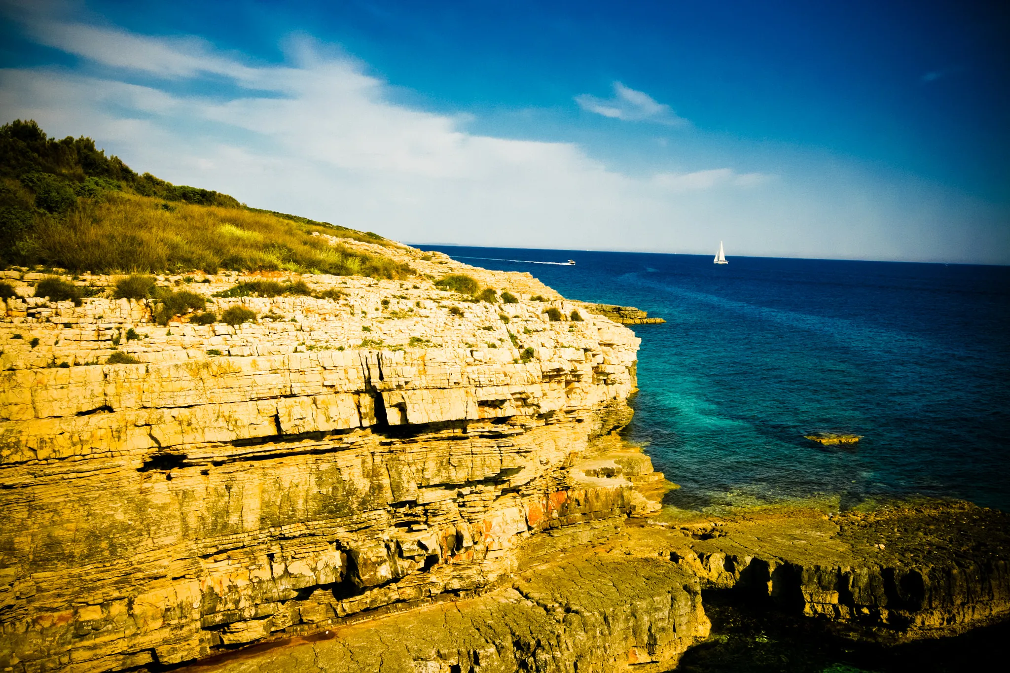 Rugged limestone cliffs dropping into the clear blue Adriatic Sea at Cape Kamenjak near Pula, Croatia