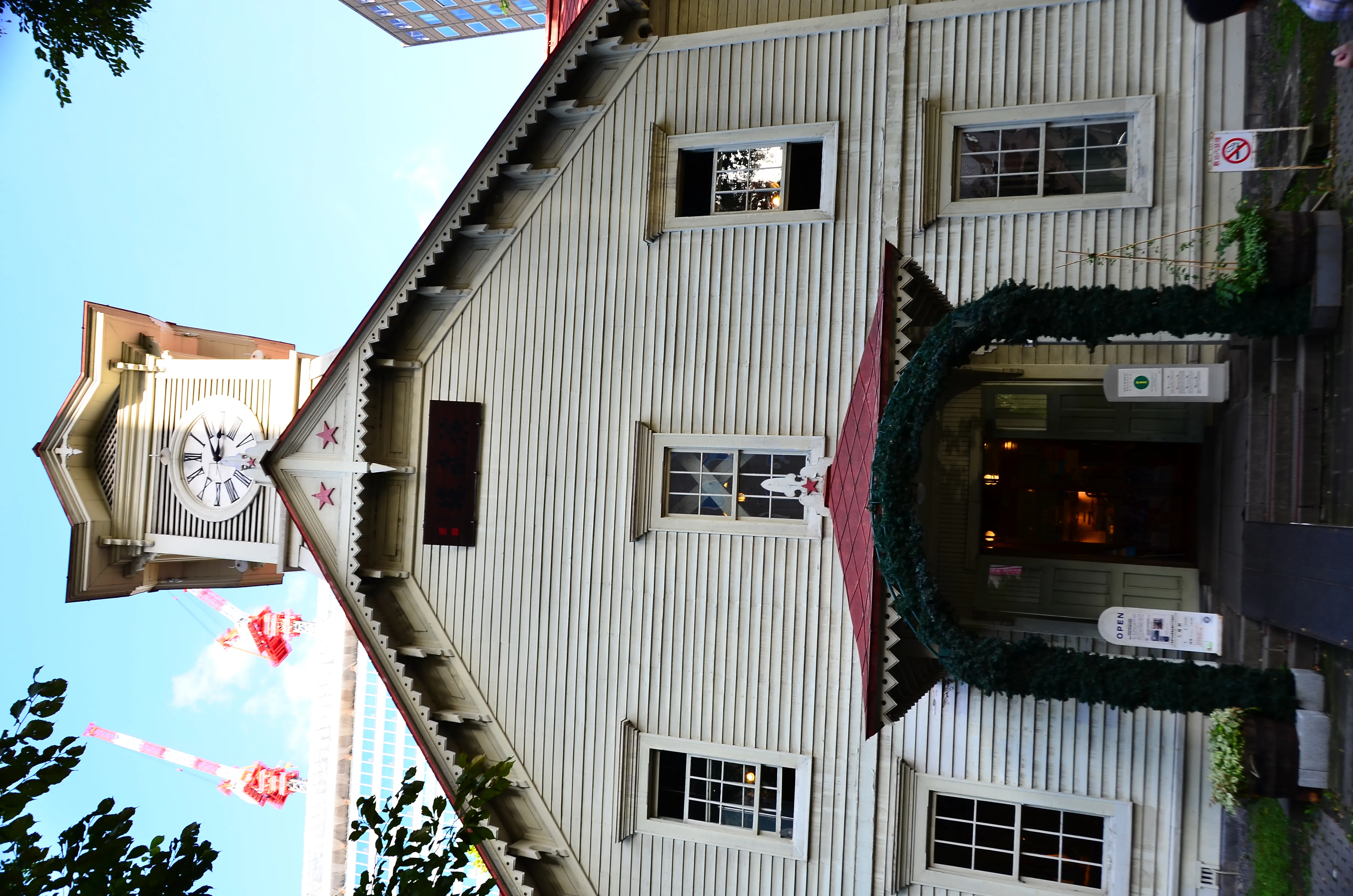 The white wooden Sapporo Clock Tower with its red roof and central clock among modern buildings