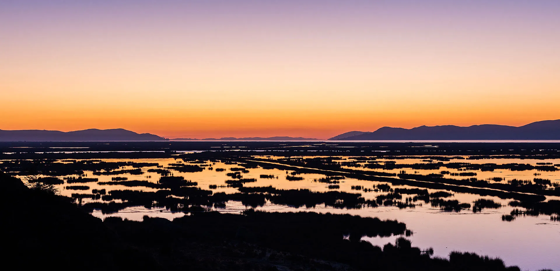 Sunrise over Lake Titicaca near Puno, golden light on the calm waters of the world's highest navigable lake