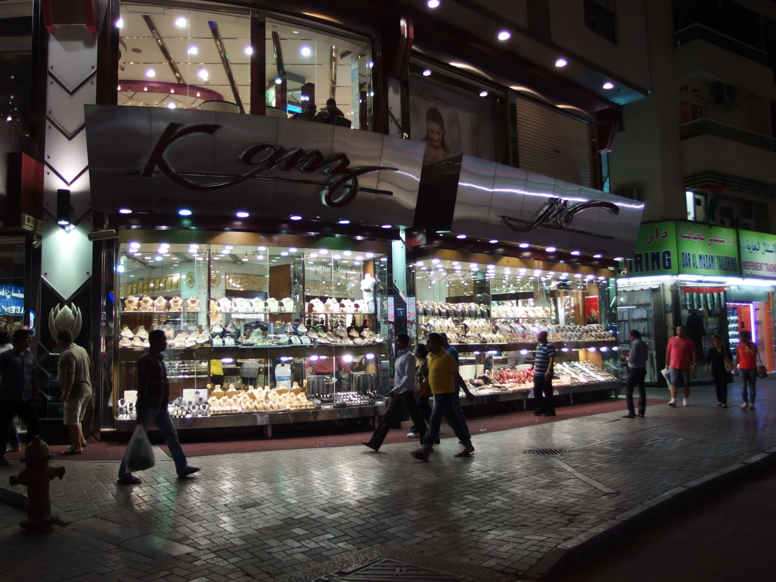 Shoppers walking past illuminated jewellery windows along a covered lane of the Dubai Gold Souk in Deira