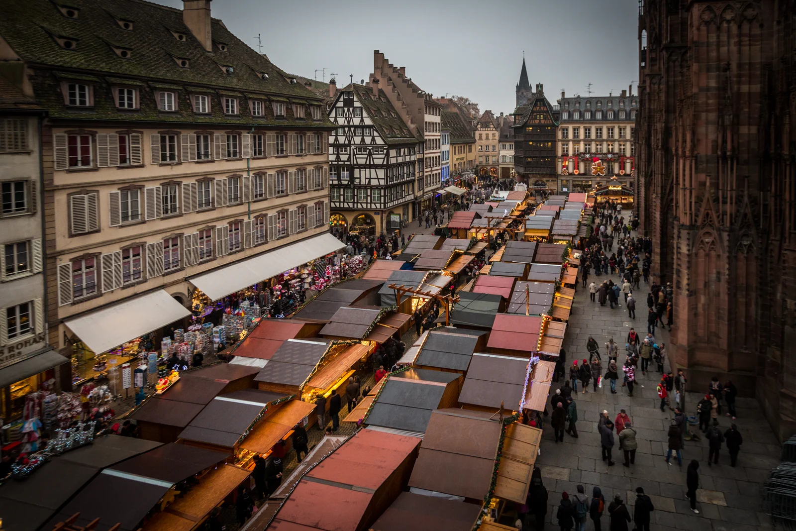 Elevated daytime view over rows of wooden market chalets on Strasbourg's Place de la Cathédrale, with half-timbered houses alongside