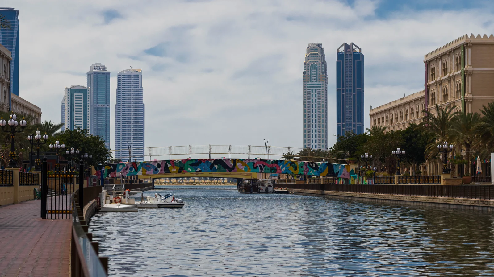 Mural-painted pedestrian footbridge over the Al Qasba canal in Sharjah, with high-rise towers behind