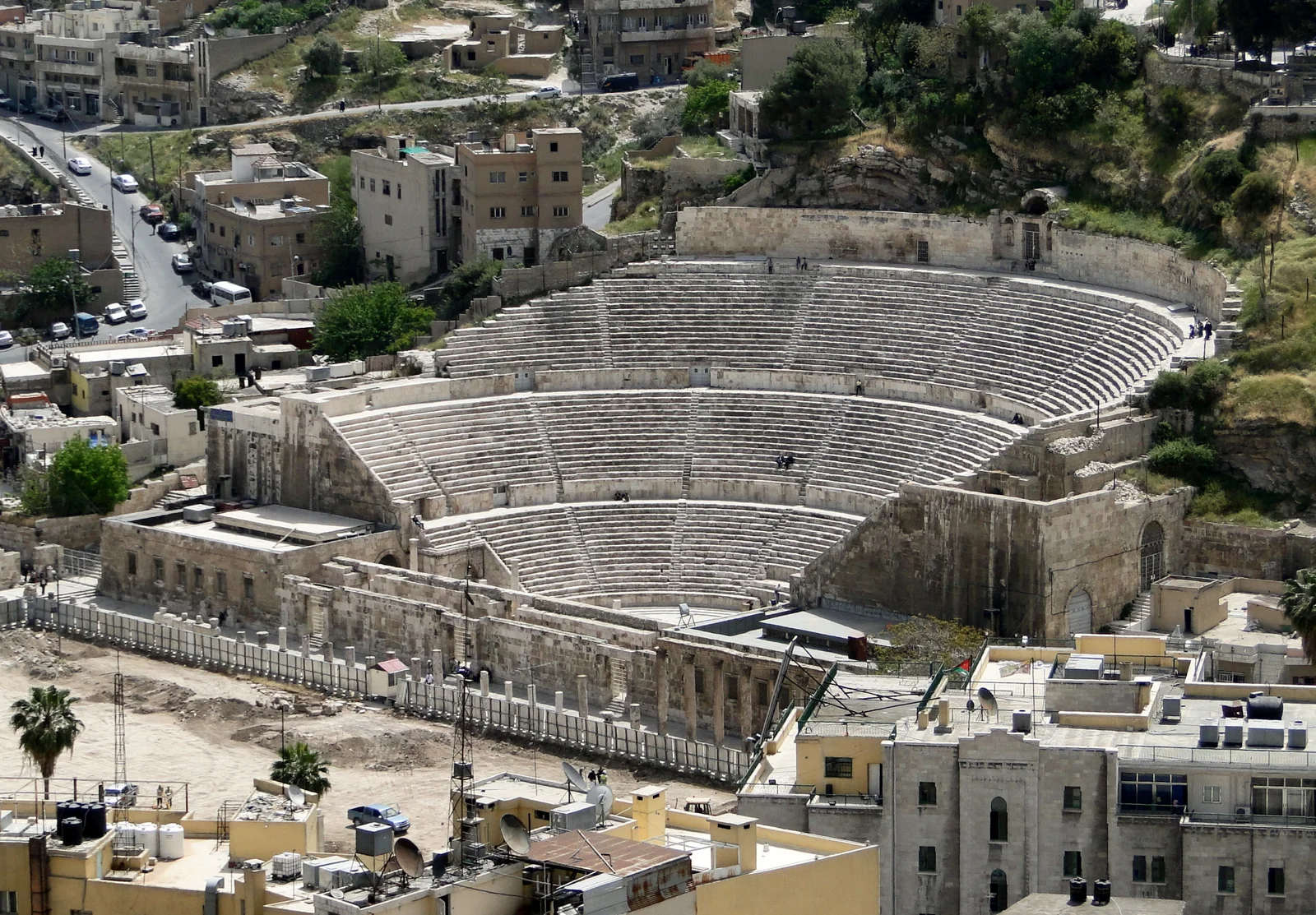 The Roman Theatre of Amman seen from above, its deep semicircular tiers of stone seating carved into the hillside and ringed by the pale buildings of the modern city