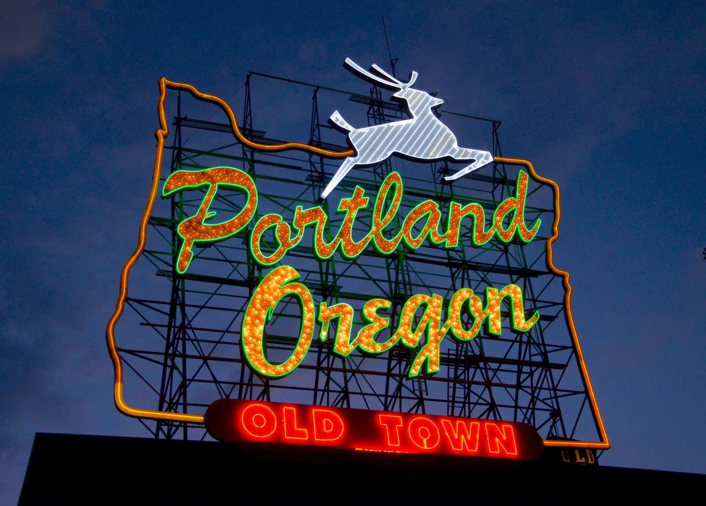 Illuminated White Stag neon sign reading Portland Oregon Old Town with a leaping white deer against a deep blue dusk sky