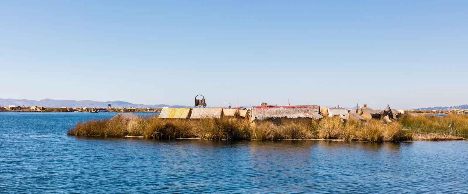 A single Uros reed island with low thatched dwellings on a golden totora platform across the blue water of Lake Titicaca