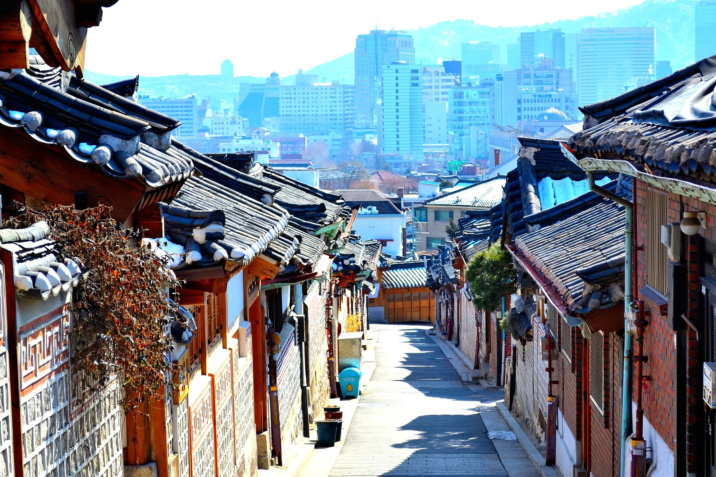 Traditional Korean hanok rooftops cascading down the hillside in Bukchon Hanok Village, Seoul, with the city skyline in the background
