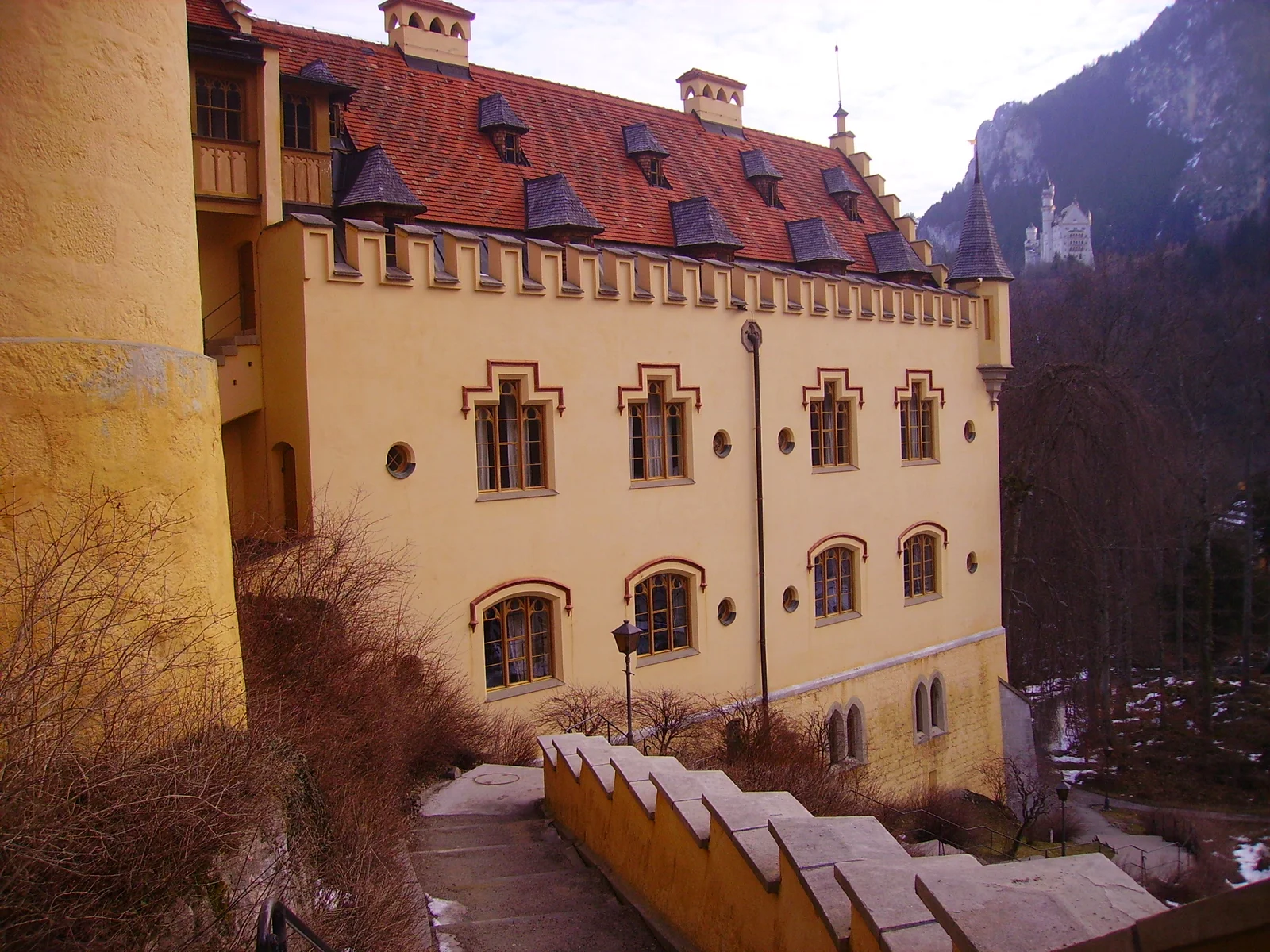 The yellow walls and towers of Hohenschwangau Castle on a wooded hill below the Bavarian Alps