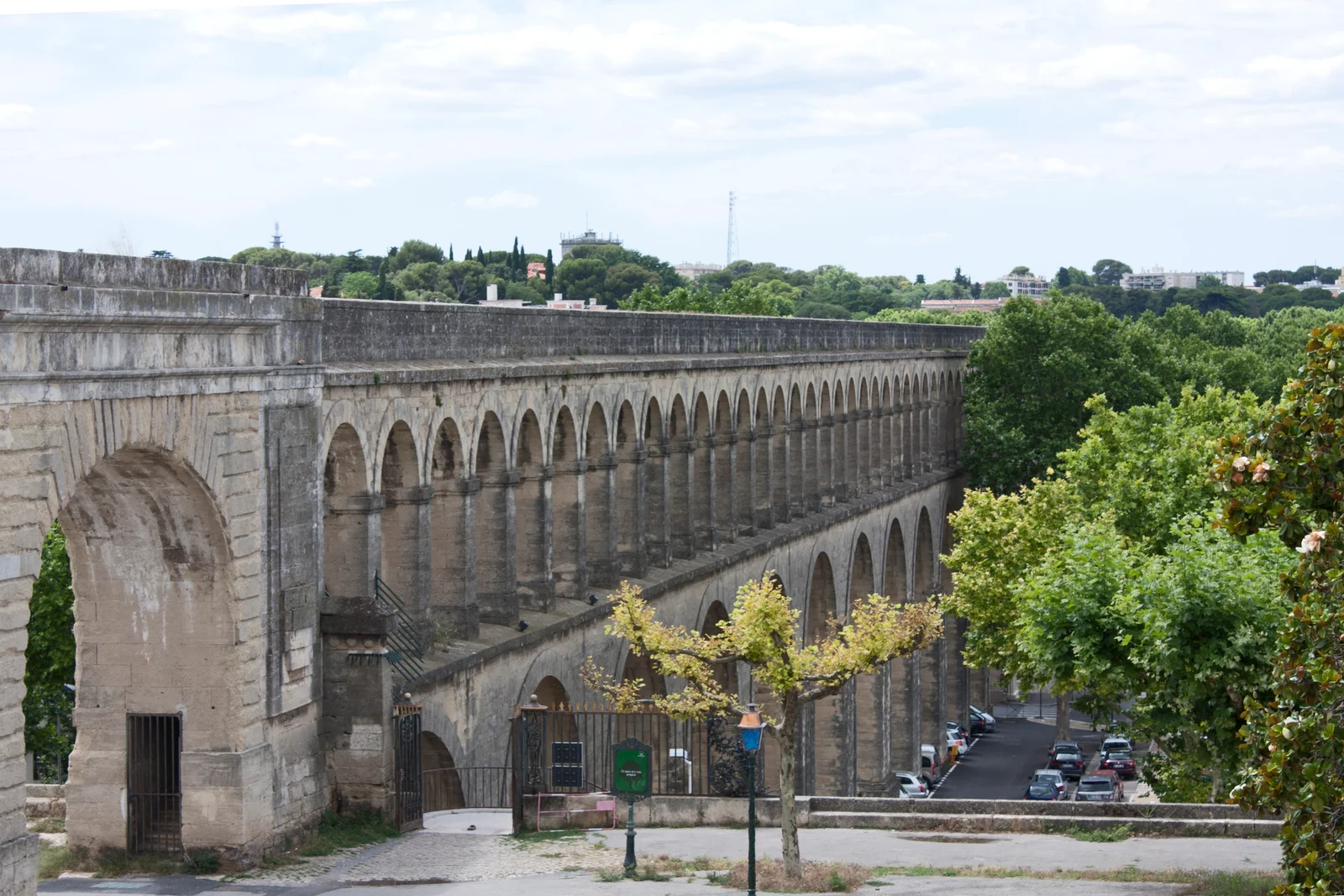 The double-tiered stone Saint-Clement aqueduct, Les Arceaux, receding into the distance beside a tree-lined street