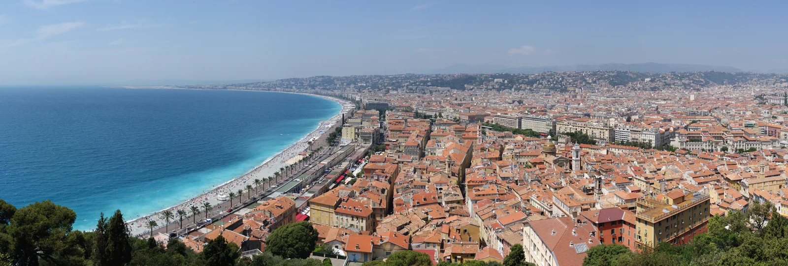 Panorama from Castle Hill over the curving Baie des Anges, with the Promenade des Anglais tracing the beach and the red-roofed old town of Nice at right