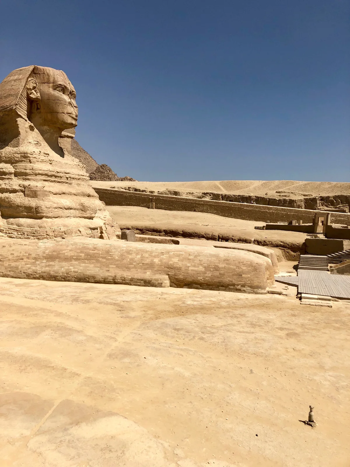 The Great Sphinx viewed from the front at an angle, its outstretched paws and reclining body under a clear blue sky