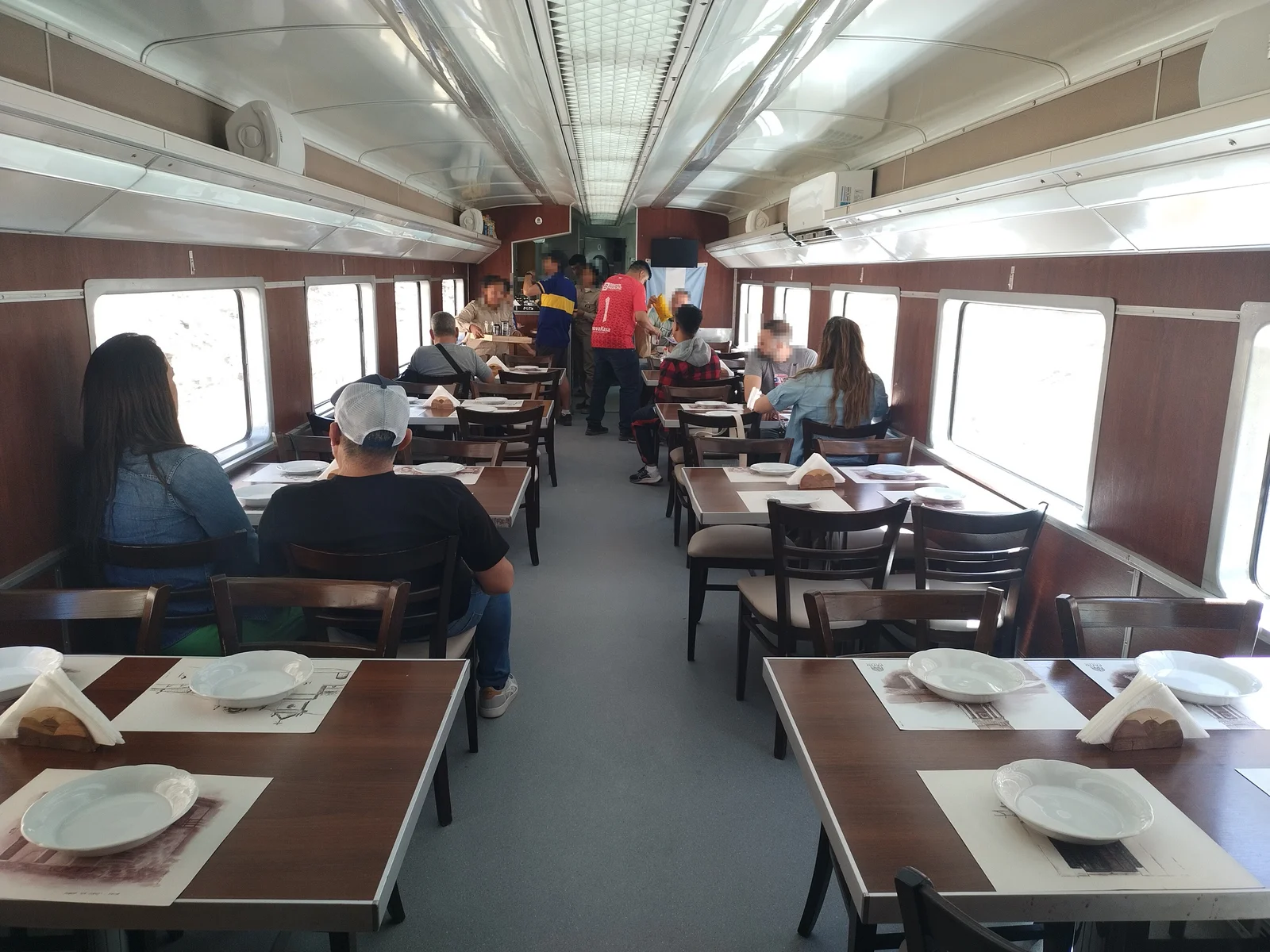 Interior of the Tren a las Nubes dining car, with wooden tables set with white plates and napkins and passengers seated beside the windows
