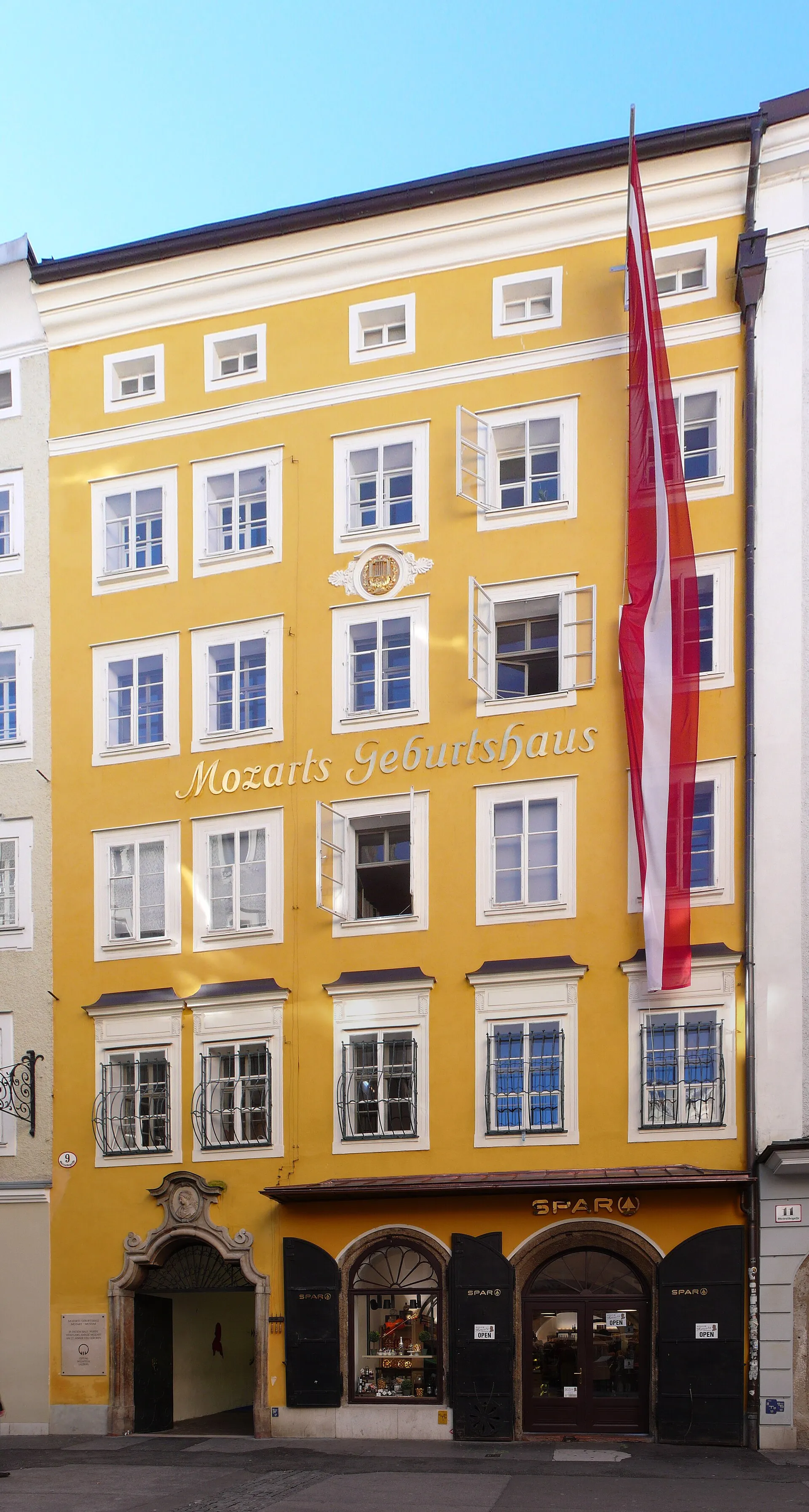 The bright yellow facade of Mozart's Birthplace at Getreidegasse 9 in Salzburg, with wrought-iron shop signs on the street